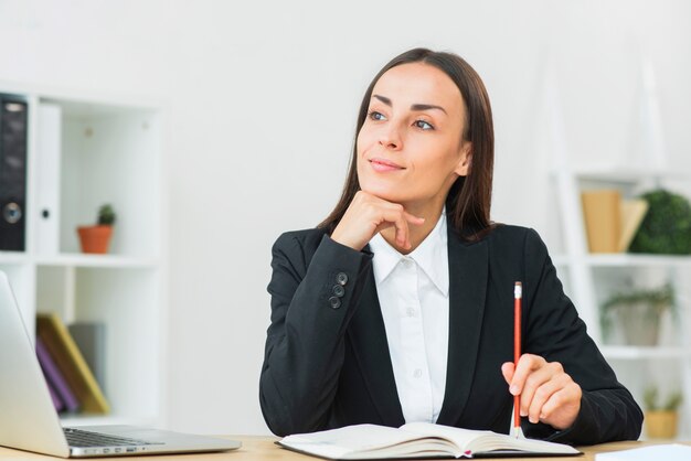 Contemplated young businesswoman holding pencil in hand on diary