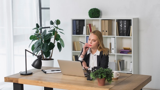 Contemplated young businesswoman looking at laptop in the office