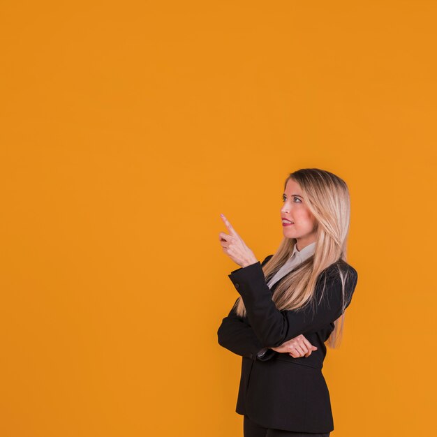 Contemplated young businesswoman pointing her finger against an orange background