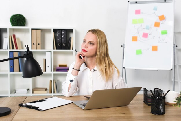 Contemplated young businesswoman with laptop on wooden table in the office