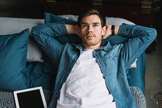 Free photo contemplated young man lying on bed looking up with digital tablet