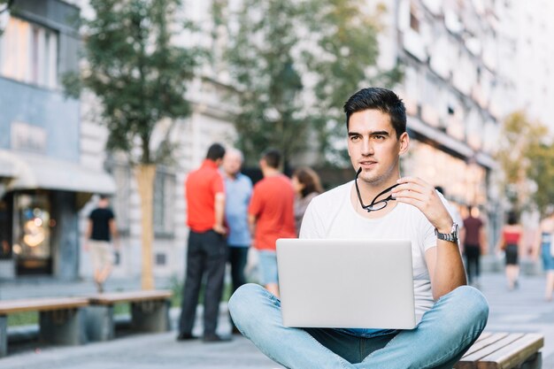 Contemplated young man sitting on bench with laptop