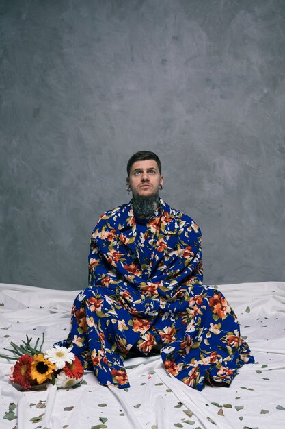 Contemplated young man sitting on floor with crossed legs near the gerbera flowers