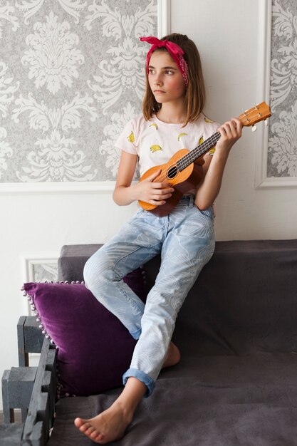 Contemplating girl holding ukulele looking away at home