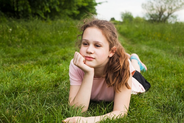 公園で緑の草の上に横たわる美少女を考えてください。
