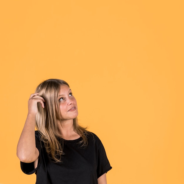 Contemplating young woman looking up over yellow backdrop