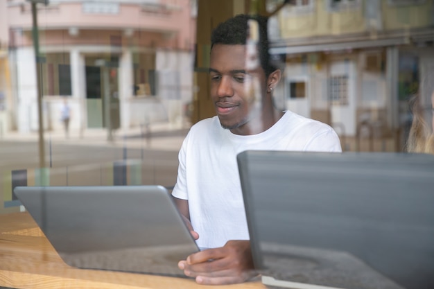 Content African American guy sitting at table and using laptop