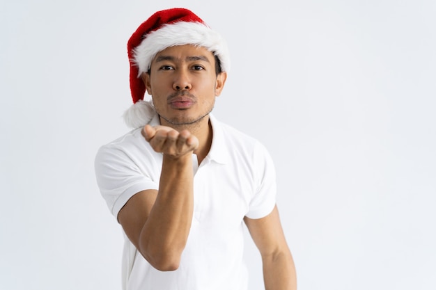 Content Asian man wearing Santa hat and sending air kiss