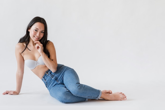 Содержимая азиатская женщина в лифчике и джинсах сидя