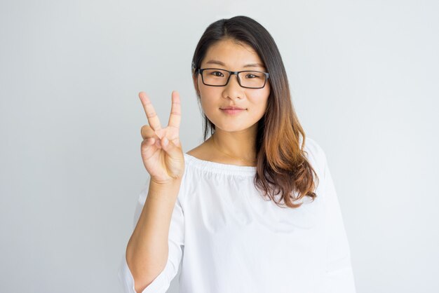 Content attractive woman in eyeglasses showing greeting gesture and looking at camera.