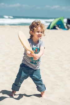 Довольный мальчик играет с ракеткой на пляже