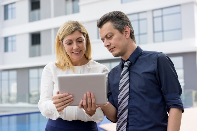 Content business people reading news on tablet computer outdoors. 