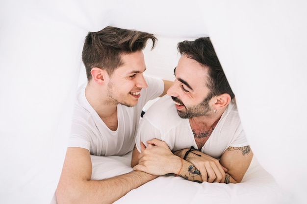 Free photo content gay couple posing playfully under blanket