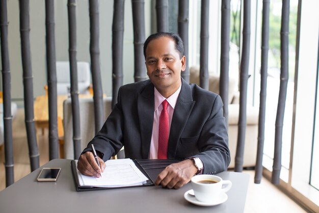 Content Indian Businessman Completing Form in Cafe