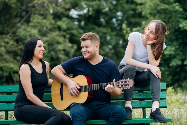 Foto gratuita persone contente seduto sulla panchina e suonare la chitarra