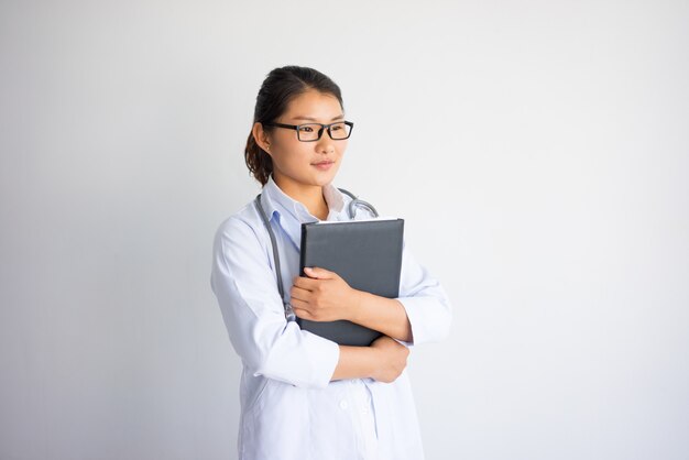 Content pretty young Asian female doctor holding folder. 