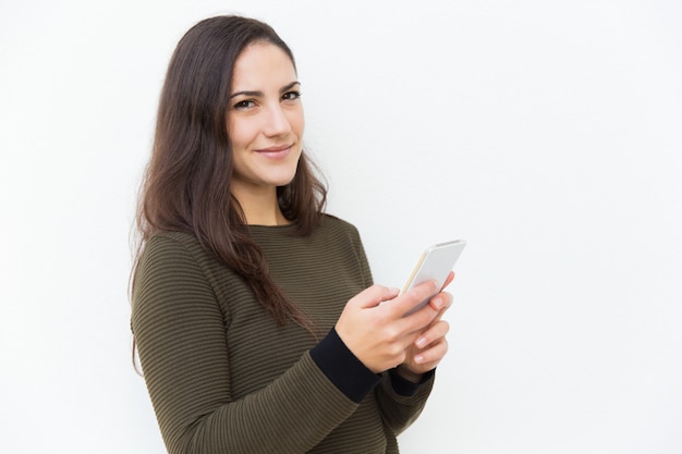 Довольная усмехаясь латинская женщина держа мобильный телефон