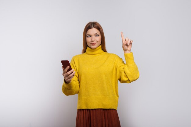 Content woman holding smartphone and pointing up