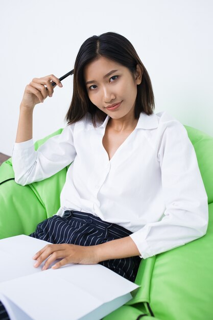 Content Woman Sitting in Beanbag Chair with Pen