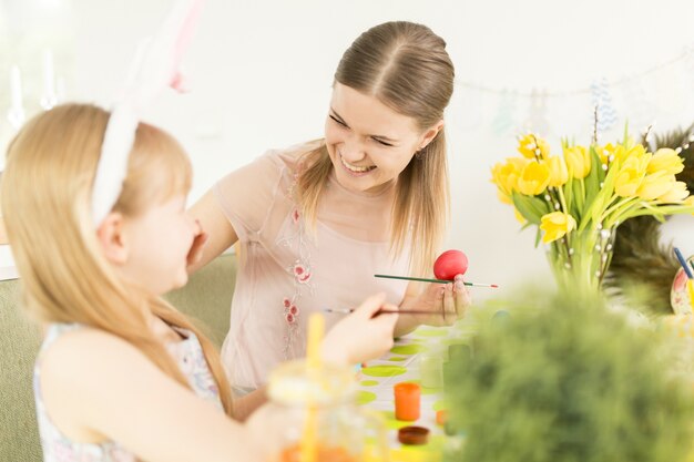 Content woman with girl preparing Easter eggs