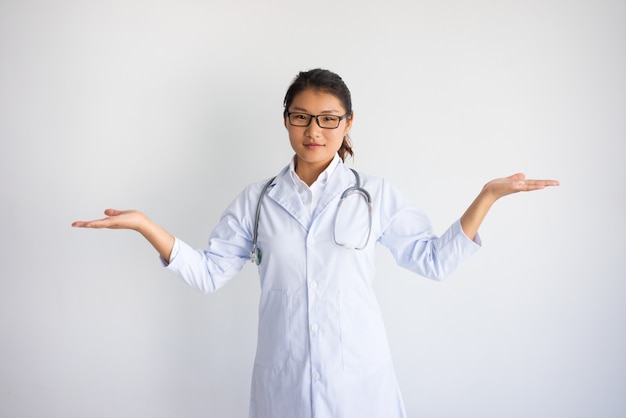 양손으로 빈 공간을 잡고 콘텐츠 젊은 아시아 여성 의사.