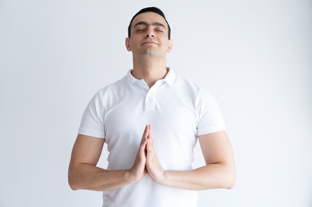 Content young man praying with his eyes closed and keeping hands together.