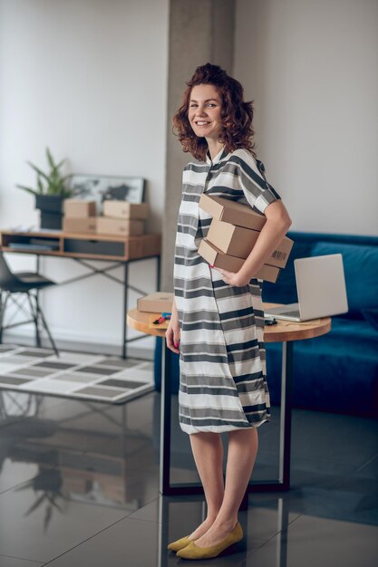 Free photo contented online store employee holding a pile of cardboard boxes