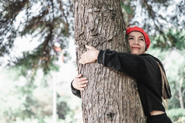 コピースペースで至福の表情で大きな木を抱き締める満足のいく若い女性環境への配慮の概念