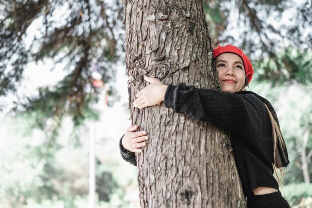 Contented young woman hugging a large tree with a blissful expression with copy space Concept of care for environment