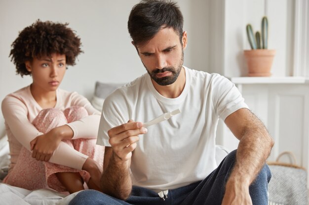 避妊は失敗し、望まない妊娠の概念。欲求不満の若い家族のカップルは妊娠検査をチェックします