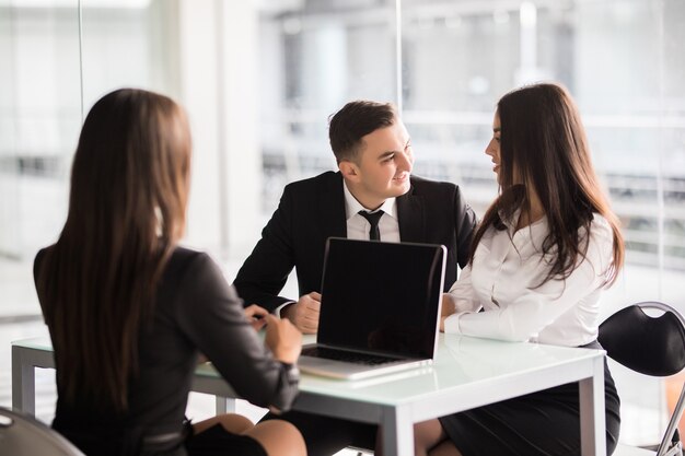 Contract with best conditions. Confident young woman explain some details of document and pointing it with smile while sitting together with young couple at the desk in office