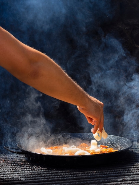 Free photo cook adding calamari rings to vegetables on frying pan