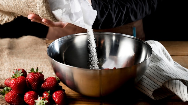 Cook adding sugar to bowl with strawberries