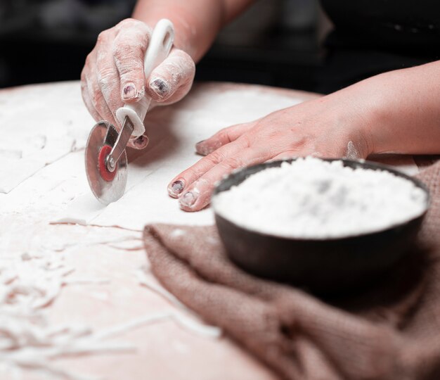 A cook cutting ravioli dough, flour in a black bowl