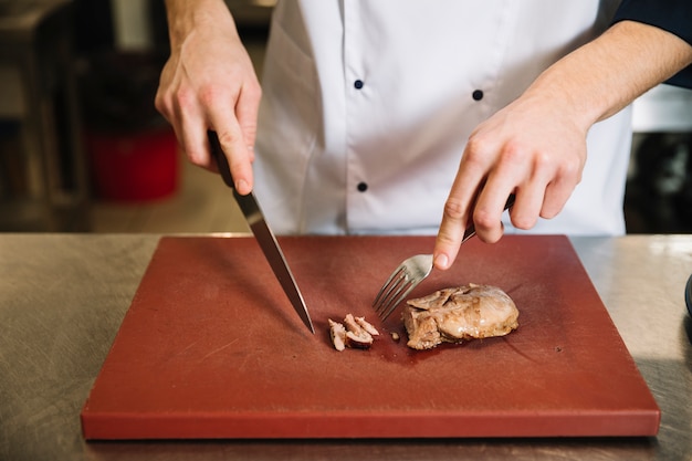 Cook cutting roasted meat on board