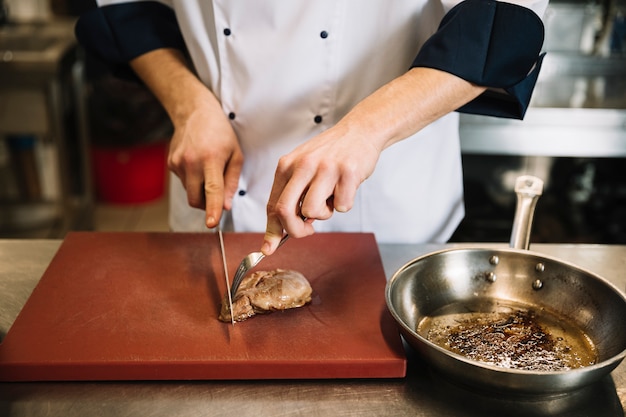 Free photo cook cutting roasted meat on wooden board