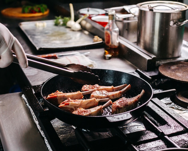 Cook frying meat ribs inside round metal pan in the kitchen