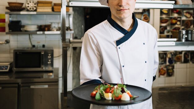 Free photo cook holding plate with vegetarian salad