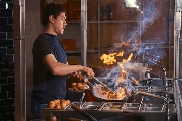 Cook is fry vegetables with spices and sauce in a wok on a flame. cooking process in an asian restaurant.