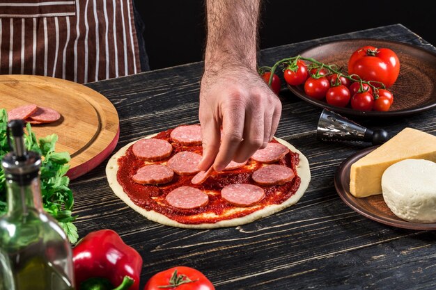 Cook in the kitchen putting the ingredients on the pizza on an old wooden background. Pizza concept. Production and delivery of food. Cooking concept. Close-up