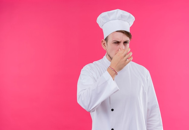 Cook looking at camera dissatisfied making smelling bad gesture standing over pink wall