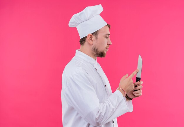 Cook looking to knife touching its standing over pink wall
