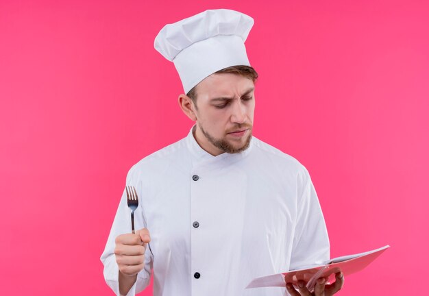 Cook looking seriously to book with chalk standing over pink wall