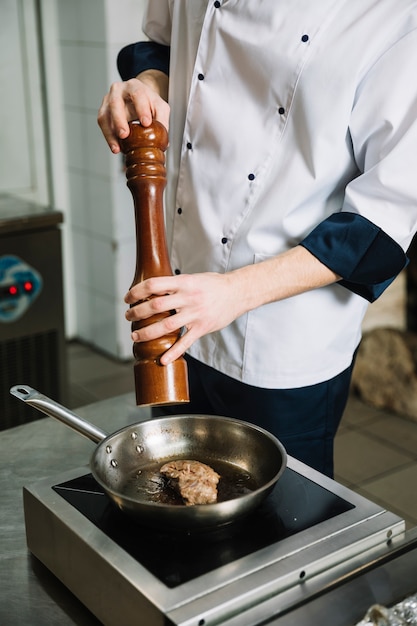 Cook peppering fried meat in pan on table