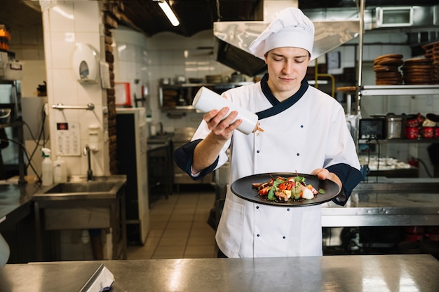 Cook pouring sauce on big plate with salad