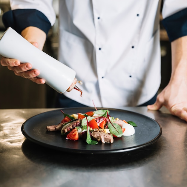 Free photo cook pouring sauce on plate with salad