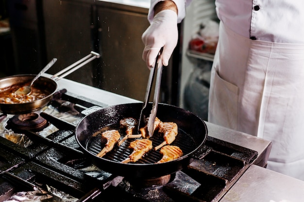 Cook preparing meat ribs inside black metal pan in the kitchen