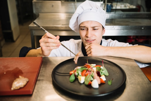 Cook preparing salad with fried meat at table