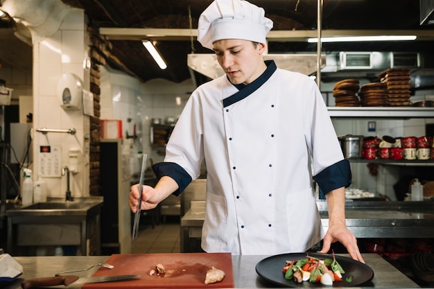 Cook preparing salad with meat in kitchen 