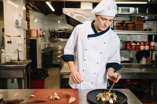 Cook preparing salad with meat at table